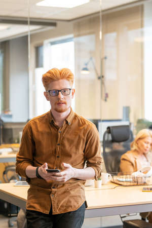 Young contemporary confident businessman in eyeglasses using mobile phoneの写真素材