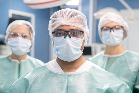Young professional male surgeon and his two assistants in protective uniformの写真素材