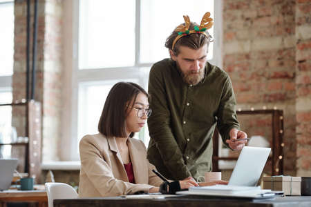 Young serious businessman with xmas headband explaining data on laptop display