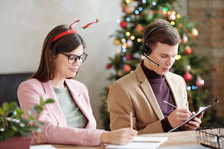 Young businessman with headset making notes and consulting clients by colleagueの写真素材