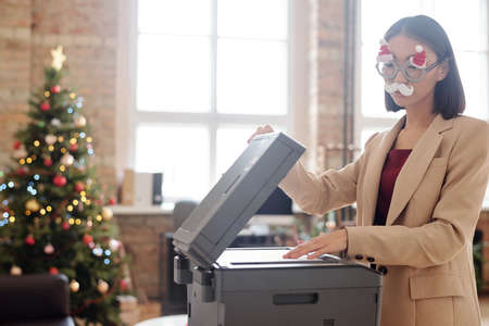 Young pretty secretary in xmas eyeglasses with white moustache standing by xerox