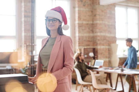 Young cheerful businesswoman in xmas cap and eyeglasses looking at youの写真素材