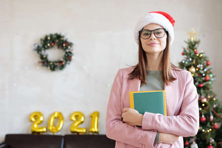 Young woman in Santa cap standing against decorated firtree and xmas wreath