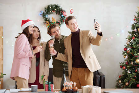 Group of young business partners with flutes of champagne making selfie