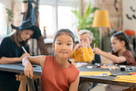 Portrait of content Asian girl sitting against teacher and children at Halloween craft classの写真素材