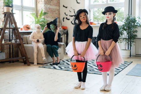 Serious multi-ethnic mimes girls in pink tutu skirts and black hats standing with trick-or-treating...