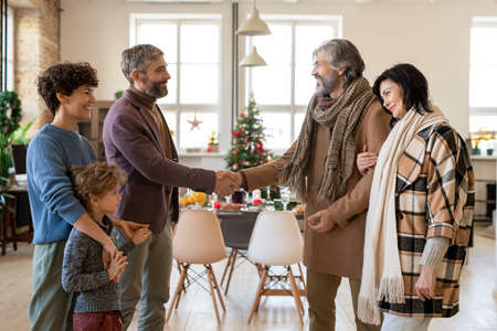 Happy young and mature couples greeting each other during Christmas visit