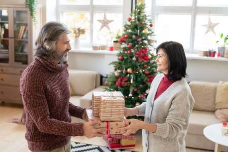 Happy mature man passing three giftboxes to his pretty wife while looking at her