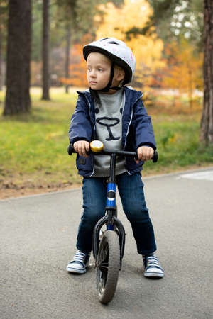 Adorable blond boy in casualwear and safety helmet standing on asphalt roadの写真素材