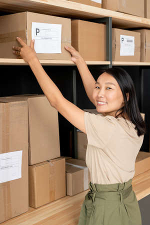 Happy young female manager taking one of packed boxes with orders of clients