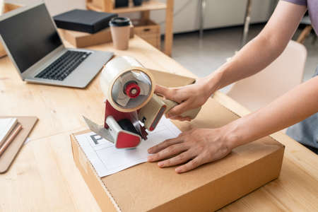 Hands of female manager of online shop sealing cardboard box with packed orderの写真素材