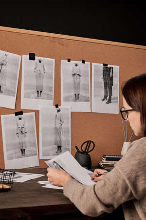 Young brunette female fashion designer working with photos in front of board