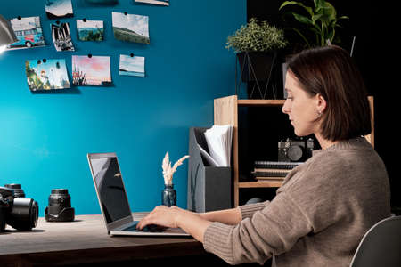 Contemporary young female designer or photographer using laptop in studio