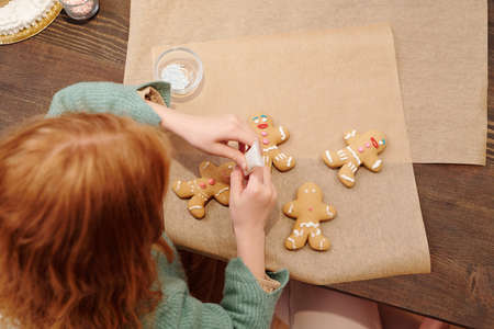 Cute little girl decorating homemade gingerbread cookies with white glazeの写真素材