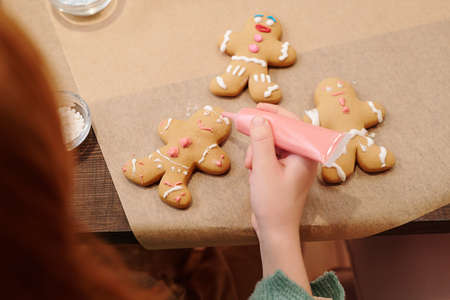 Hand of little girl decorating homemade gingerbread cookies with pink glaze