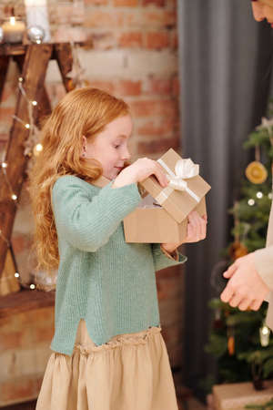 Surprised little girl in casualwear opening giftbox with Christmas presentの写真素材