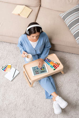 Young female designer in blue pajamas and headphones working on the floor