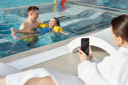 Young man and his laughing little daughter playing together in swimming pool
