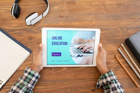 Top view of hands of elementary schoolboy watching online lesson by table