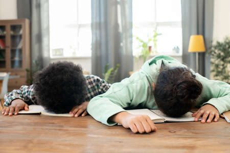 Tired elementary girl and boy in casualwear lying on their open copybooks