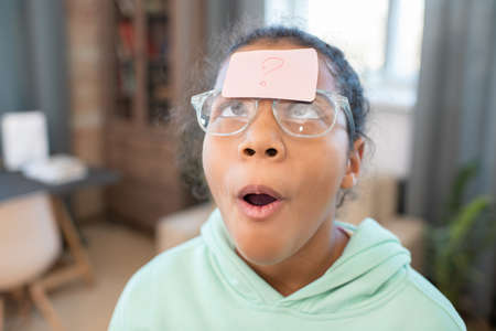 Girl in eyeglasses looking at notepaper with question mark on her forehead