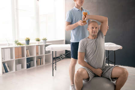Bald athlete in activewear exercising on medical couch in rehabilitation clinicsの写真素材