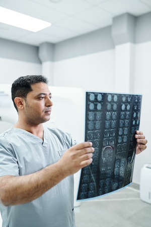 Confident male radiologist in uniform looking at x-ray image of one of patientsの写真素材