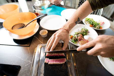 Hands of young male chopping piece of smoked or grilled beef on special boardの写真素材