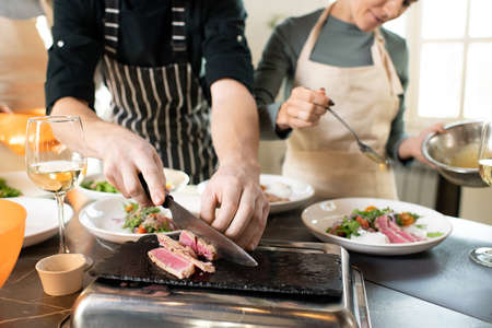 Hands of young male cooking coach chopping piece of smoked beef by tableの写真素材