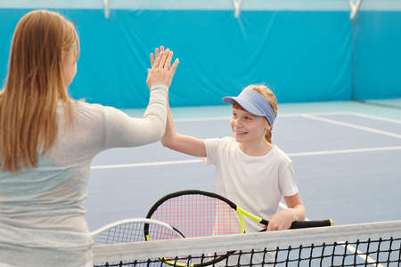Happy girl in activewear holding tennis racket while giving high five to trainer