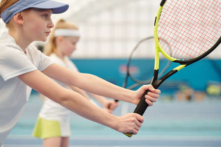 Serious and concentrated teenage girl with tennis racket standing on stadiumの写真素材
