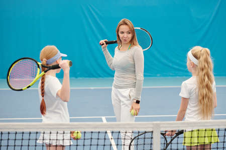 Young confident tennis trainer in activewear consulting two girls on stadiumの写真素材