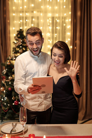 Young cheerful elegant couple waving hand and communicating in video chatの写真素材