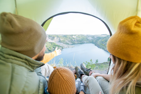 Young man talking to little son sitting between parents while family having restの写真素材