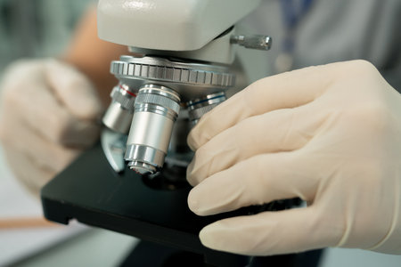 Gloved hand of contemporary worker of scientific laboratory fixing metallic lensの写真素材