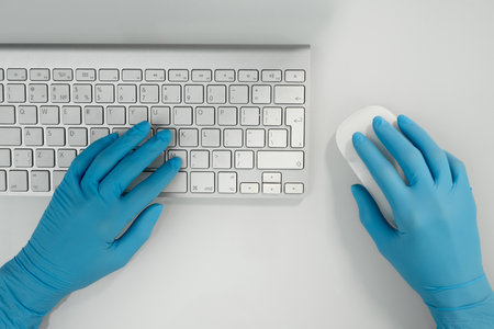 Overview of gloved hands of contemporary medical worker clicking computer mouseの写真素材