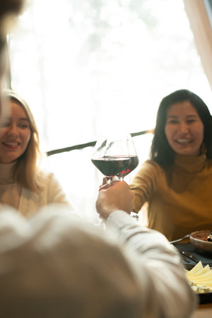 Young cheerful Asian woman clinking with glass of red wine with her boyfriendの写真素材