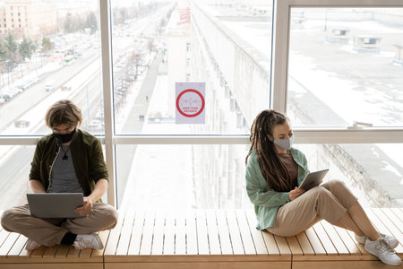 Two office workers sitting by window with announcement about keeping distanceの写真素材