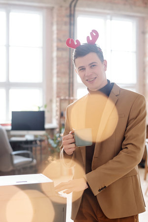 Cheerful businessman in xmas headband looking at you and having coffeeの写真素材