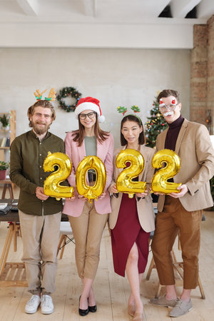 Several colleagues in xmas accessories holding inflatable numbers of new year