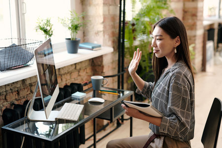 Young female manager in casualwear waving hand to people on computer screenの写真素材