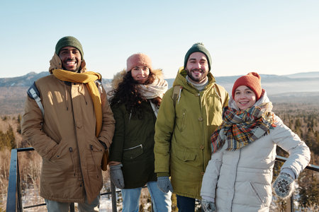 Happy young intercultural friends in winterwear standing against mountainsの写真素材