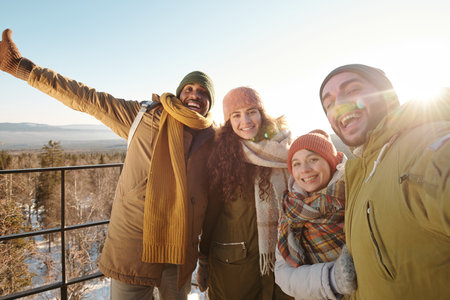 Excited intercultural friends in winterwear making selfie against sunshine