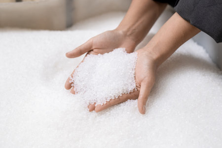 Hands of young female worker holding pile of unprocessed white plastic pelletsの写真素材