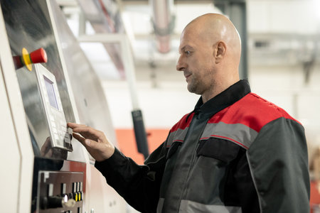 Mature worker of polymer processing factory pressing button on control panel