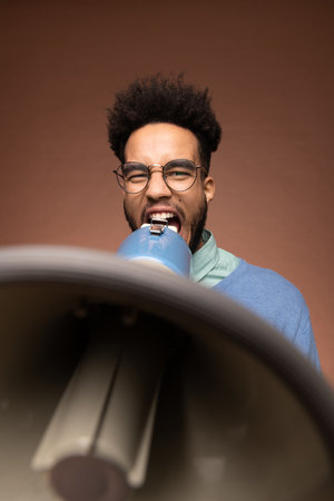 Young furious mixed-race businessman or boss in eyeglasses shouting in megaphoneの写真素材