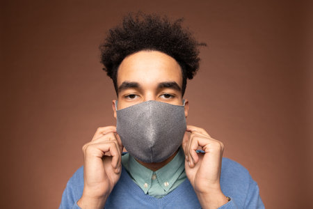 Young contemporary mixed-race businessman in smart casualwear and protective mask looking at you while standing in front of cameraの写真素材