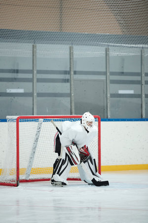 Hockey player in white sports uniform, helmet, gloves and skates holding stickの写真素材