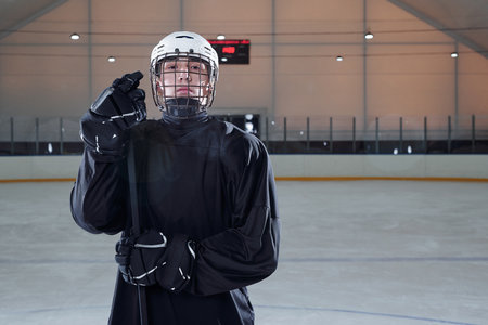 Serious male hockey player in black sports uniform, gloves and protective helmet