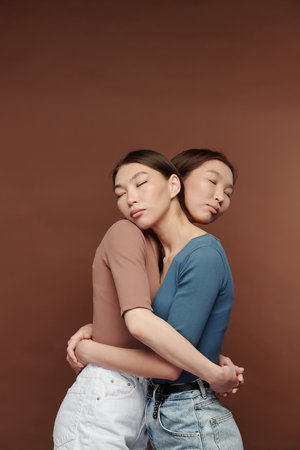 Two young affectionate female twins of Asian ethnicity standing in embraceの写真素材